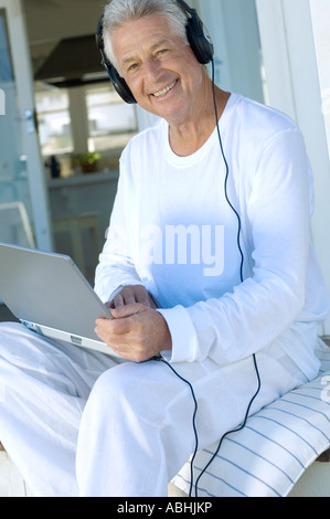 Uomo sorridente con cuffie utilizzando laptop Foto Stock