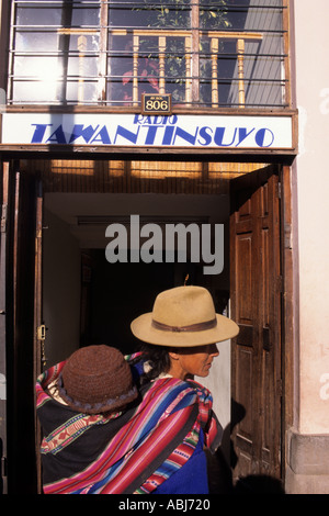 Cusco, Perù. Donna in abiti tradizionali di trasportare un bambino sulla schiena, Cusco stazione Radio è in background. Foto Stock