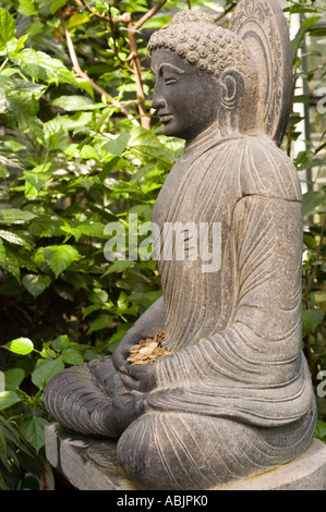 Statua in pietra del Buddha che medita a Bodhgaya sotto l'albero di Bodhi per raggiungere l'illuminazione, con monete in grembo e sfondo verde fogliame. Foto Stock
