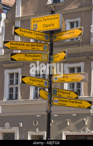 Cartello stradale che mostra la direzione e le distanze per le città partner nella piazza del mercato di Opole, Slesia, Polonia. Segnali direzionali gialli su un palo. Foto Stock