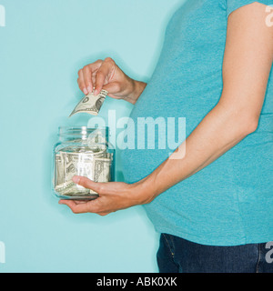 Donna incinta mettere soldi in vaso Foto Stock