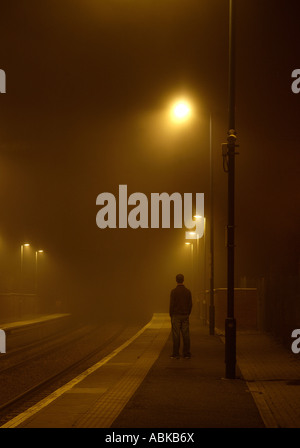 Un uomo in piedi con speranza a un nebbioso stazione ferroviaria. Foto Stock