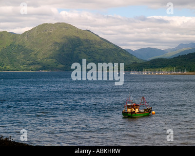 Un piccolo verde e giallo pesca barca ormeggiata in loch Creran con un porto turistico e le colline alle spalle di Highlands della Scozia UK Foto Stock