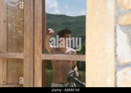 Un ritratto di una riflessione di un giovane uomo con una telecamera in una finestra di una tradizionale villa in Toscana, Italia. Foto Stock