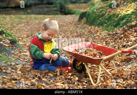 Po' ragazzo seduto in marrone caduto foglie di autunno Foto Stock
