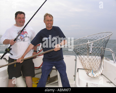 Il pescatore e Skipper con un bel Bass in net catturati nel Solent REGNO UNITO Foto Stock