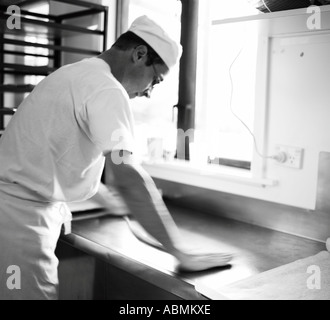 Il panettiere maschio in panetteria pane brezels nella piccola cucina commerciale rolling out prima di metterli su vassoi da forno Foto Stock