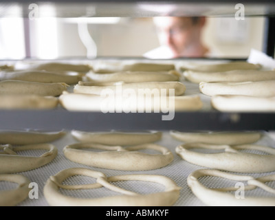 Il panettiere maschio in panetteria pane brezels nella piccola cucina commerciale collocato su vassoi da forno a salire Foto Stock