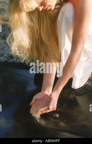 Donna bionda immergendo le mani nel piccolo ruscello in Svezia Foto Stock