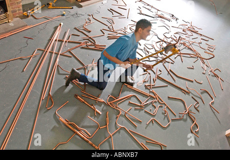 Un giovane apprendista Gas Service Engineer mettere in pratica le sue abilità con rame macchine curvatubi Foto Stock