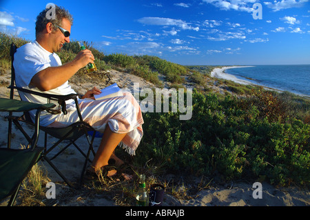 Guardare il sole andare giù la sera con una birra e un libro Foto Stock