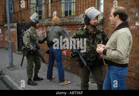 Truppe britanniche i Troubles 1980, soldati dell'esercito britannico armati a piedi di pattuglia, fermano e perquisiscono uomini in strada. Belfast Irlanda del Nord 1981 Regno Unito. Foto Stock