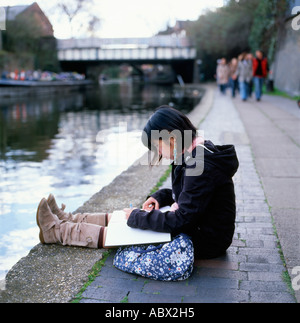 Cinese arte femmina studente seduto sul disegno la strada alzaia dal Regents Canal in Camden Lock in autunno Londra Inghilterra KATHY DEWITT Foto Stock