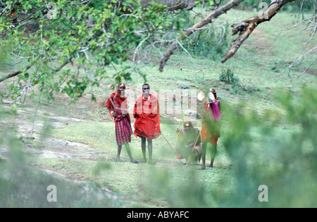 AFRICA Kenia Masai Mara riserva nazionale Masai guerrieri in rosso tradizionale abbigliamento visto attraverso gli alberi vicino il manyatta Foto Stock