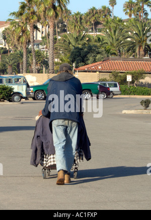 Un uomo senza tetto spinge il suo carrello tenendo i suoi beni attraverso un parcheggio in California. Stati Uniti d'America. Foto Stock