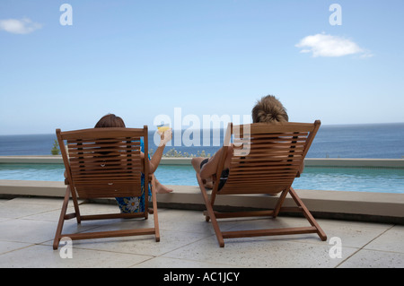 Giovane seduto in sedie a sdraio alla piscina Foto Stock