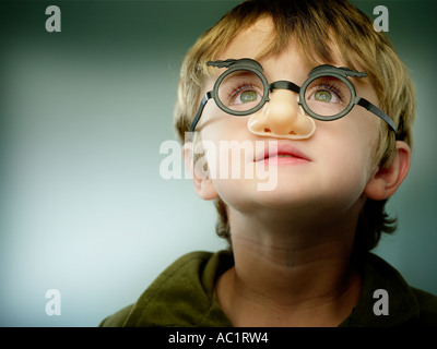 Ragazzo giovane vestito in falsi occhiali e naso cercando fino alla luce Foto Stock