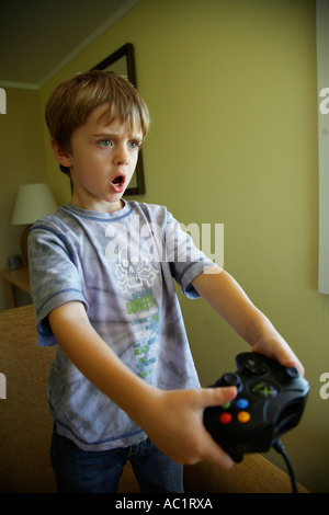 Ragazzo giovane 6yrs playing games console in piedi e concentrando guardando lo schermo in salotto Foto Stock