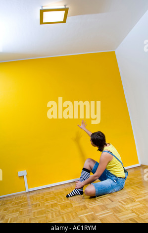 Donna seduta sul pavimento, guardando alla parete gialla Foto Stock