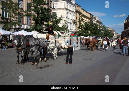 Coda di rango di turista carrozze trainate da cavalli in Rynek Glowny old town square stare miasto Cracovia Foto Stock