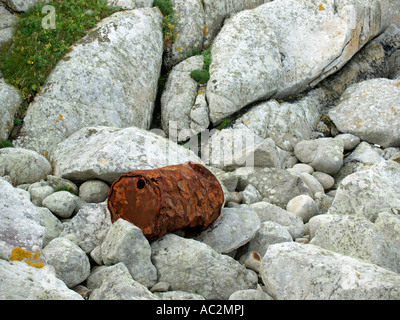 Vecchio arrugginito olio può barrell giacente sulla rocciosa costa sassosa in Bretagna Francia Foto Stock