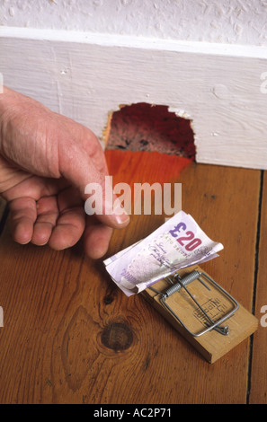 Mano protesa a prendere soldi immessi sul mousetrap invece di formaggio al di fuori mousehole in casa Foto Stock