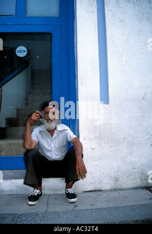 Cubano vecchio seduto davanti a un vetro blu fumo porta un tubo Foto Stock
