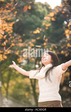 Giovane donna gettando caduta foglie Foto Stock