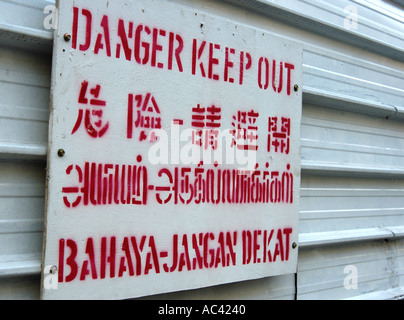 Cartello Danger Keep out stampato in inglese, cinese, tailandese e indonesiano. In un cantiere a Singapore. Foto Stock