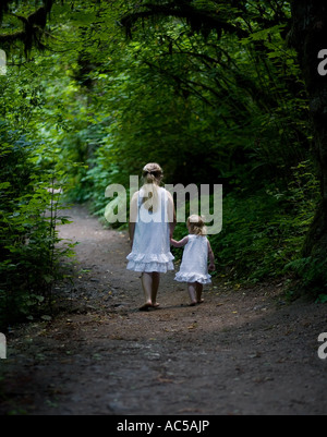 Due sorelle vagare attraverso il bosco in abiti bianchi, tenendo le mani a piedi giù per un percorso di avvolgimento Foto Stock