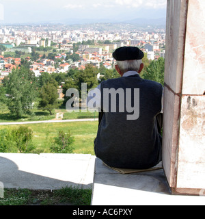 Città di Tirana nella Repubblica di Albania scompostamente fuori al di sotto di un vecchio uomo seduto sulla parete affacciata sul paesaggio urbano dalla collina nel Parco formale Foto Stock