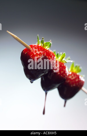 Tre le fragole su uno spiedino di kebab immerso in una fontana di cioccolato Foto Stock