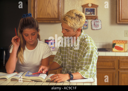 Un adolescente ragazzo con i capelli decolorati indossando un plaid shirt è rivolto a un libro di scuola che mostra una giovane ragazza teen qualcosa Foto Stock