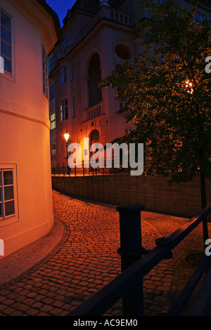 Vista notturna di una strada acciottolata di Praga, illuminata da lampioni e circondata da edifici storici e da un albero. Foto Stock