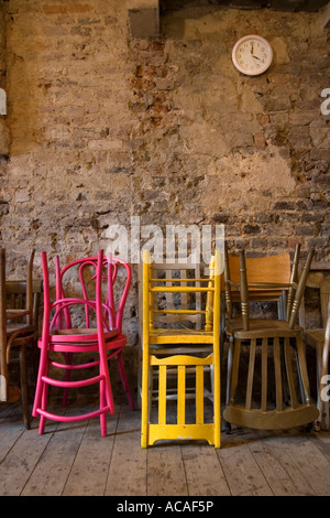 Colorate sedie di legno impilate contro un senza rendering un muro di mattoni con un orologio moderno al di sopra di esse Foto Stock