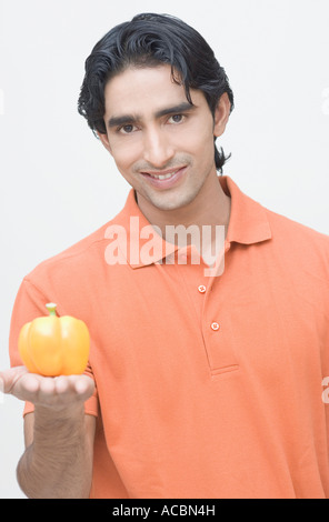 Ritratto di un giovane uomo tenendo un peperone giallo e sorridente Foto Stock