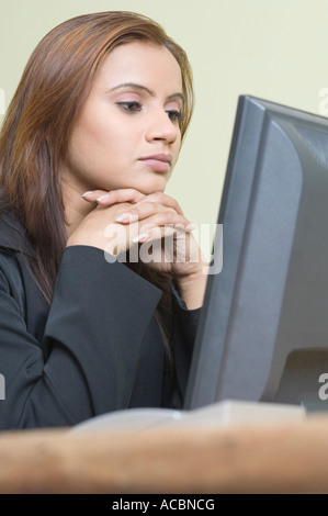 Profilo laterale di una imprenditrice seduto davanti a un computer con la mano sotto il suo mento Foto Stock