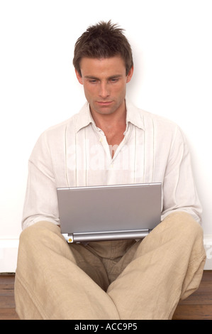 Uomo seduto sul pavimento di legno utilizzando un computer portatile in argento Foto Stock