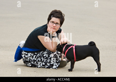 Donna seduta sul terreno e Petting Black Pug Cherokee Park Louisville Kentucky Foto Stock