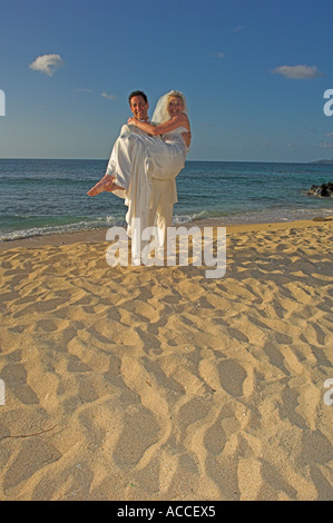 Lo sposo che trasportano sposa caldo sulla spiaggia di sabbia dorata nel tardo pomeriggio Foto Stock