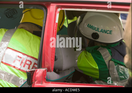 Ambulanza paramedico trattare un incidente di macchina vittima dall'interno della vettura mentre i vigili del fuoco tagliare il tetto a districarsi il conducente in modo sicuro Foto Stock