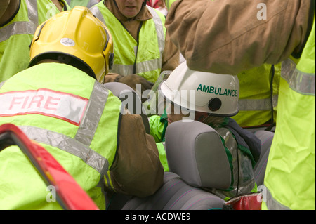 Ambulanza paramedico trattare un incidente di macchina vittima dall'interno della vettura mentre i vigili del fuoco tagliare il tetto a districarsi il conducente in modo sicuro Foto Stock