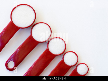 Rosso Cinque misurini riempita con sale disposte in una fila in ordine decrescente su sfondo bianco Foto Stock