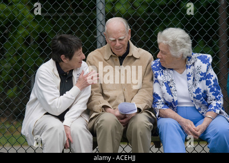 Tre anziani pensionati alti la gente seduta su una panchina e parlando in animata conversazione Foto Stock