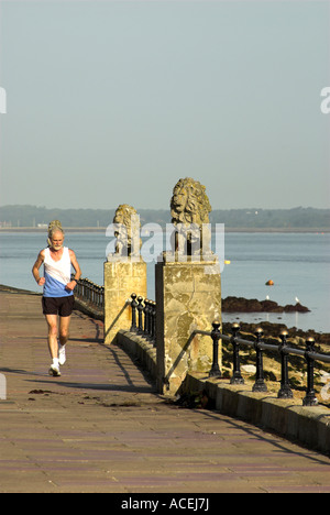 Un runner passa statue in pietra di leoni su Espalnade a Cowes sull'Isola di Wight. Foto Stock