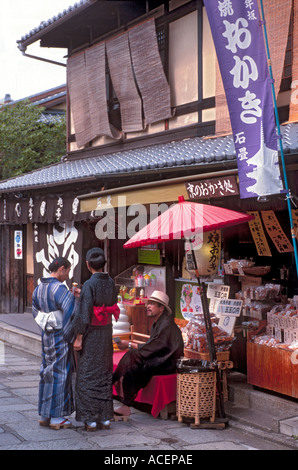 I turisti che indossa estate yukata stop per chattare con uomo in appoggio sul banco nel distretto storico di Kyoto Foto Stock