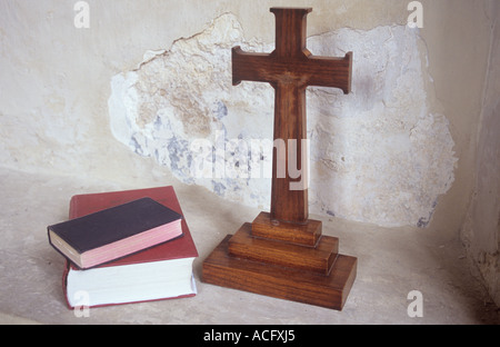 Close up di legno semplici crocifisso autoportante con inno o libri di preghiera o la bibbia in un'alcova con frantumazione di rendering di cemento Foto Stock