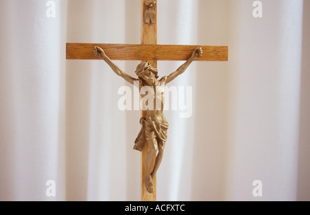 Close up di Gesù Cristo su un crocifisso in legno di fronte le pieghe di un pallido bianco crema cortina o un telo Foto Stock