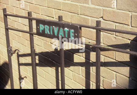 Dettaglio della pianura porta di metallo con segno indicante privato e la fusione di una profonda ombra su una pianura brickwall pallido Foto Stock