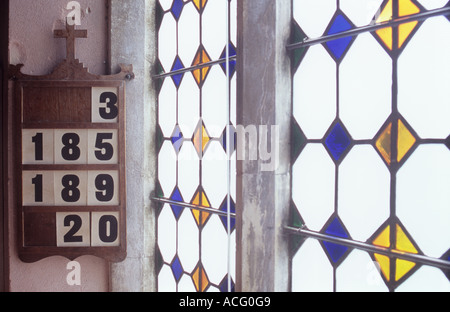 Scheda selezionata Indica i numeri di inno appeso alla parete rosa accanto a frosted leaded windows con dei diamanti colorati inserti sagomati Foto Stock